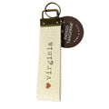 A beige key fob with the text 'virginia' written on it, along with a small heart symbol. The fob has a keychain attachment and a brand tag attached to it.