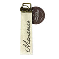 A beige canvas key fob with the brand name 'Manassas' embroidered in black script, attached to a metal keyring.