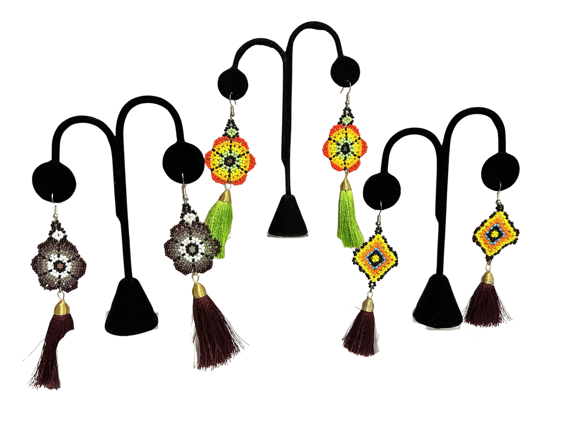 A set of handmade beaded earrings displayed on black T-shaped jewelry stands against a solid white background. The earrings feature colorful geometric and floral beadwork with tassels in brown, green, yellow, orange, and silver.