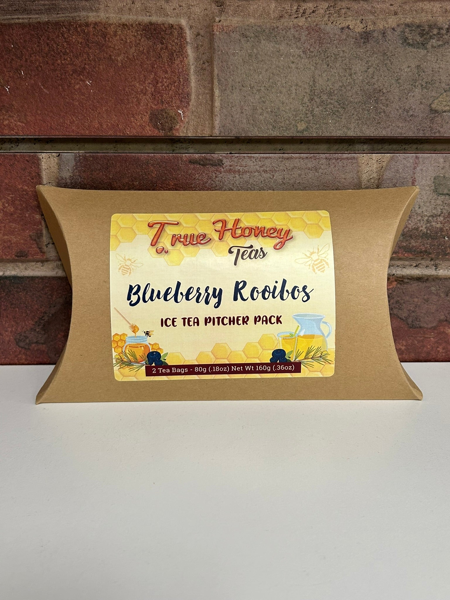 Tea package with a 'True Honey Blueberry Rooibos' label on a brick wall background