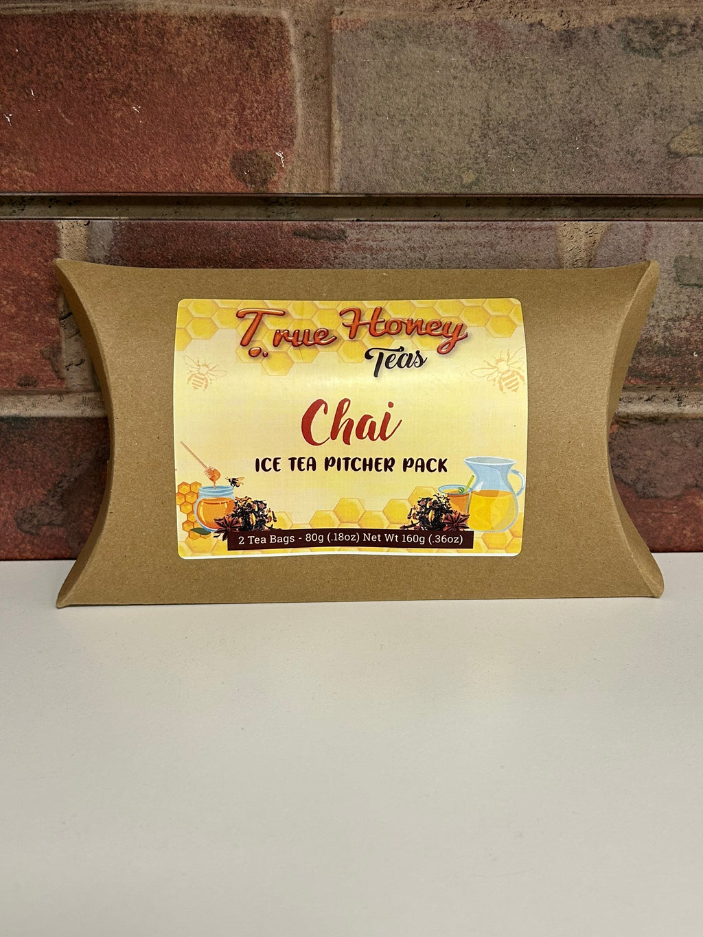 Pillow-shaped packaging with a label for True Honey Tete's Chai Ice Tea Pitcher Pack against a brick wall background.