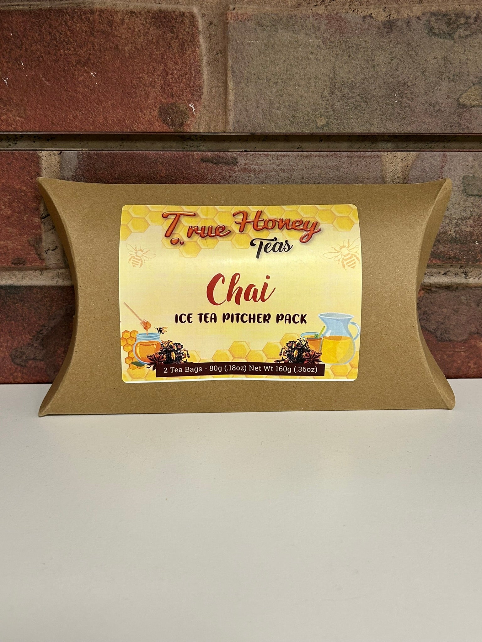 Pillow-shaped packaging with a label for True Honey Tete's Chai Ice Tea Pitcher Pack against a brick wall background.