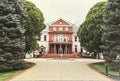 A rectangular art print or postcard showing a grand red brick mansion surrounded by tall green trees and a paved driveway.
