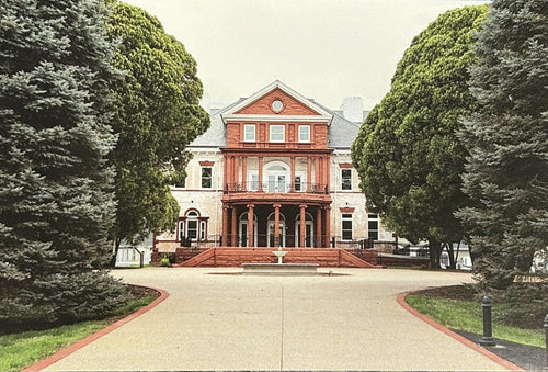 A rectangular art print or postcard showing a grand red brick mansion surrounded by tall green trees and a paved driveway.