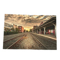A rectangular art print depicting a scenic train station platform with two tracks under a dramatic sunset sky