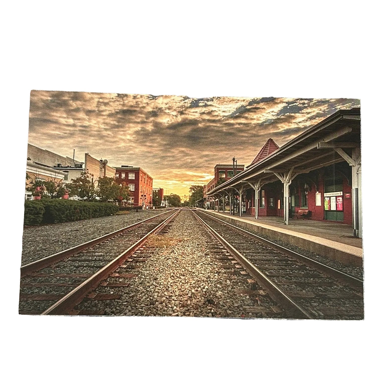 A rectangular art print depicting a scenic train station platform with two tracks under a dramatic sunset sky