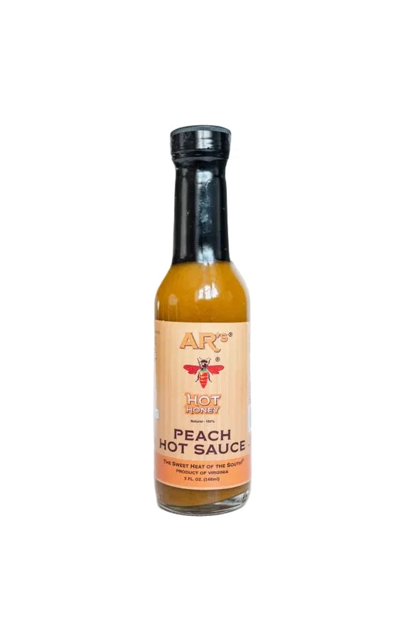 A bottle of Ar's Hot Honey Peach Hot Sauce on a clean white background. The clear glass bottle shows the amber-orange sauce inside, topped with a black cap and featuring a peach-colored label with a bee logo.
